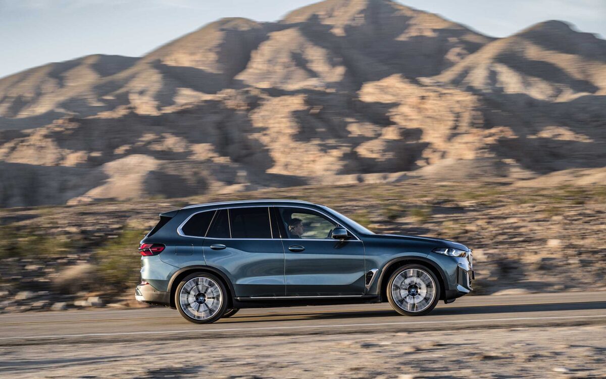 BMW X5 in blue driving along a desert road, side profile