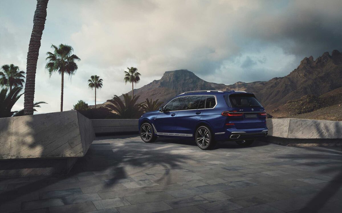 BMW X7 in blue, rear three-quarter view beside palm trees