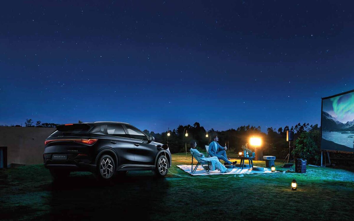 BYD Atto 3 in black seen from the rear three-quarter at night beside an outdoor movie screen