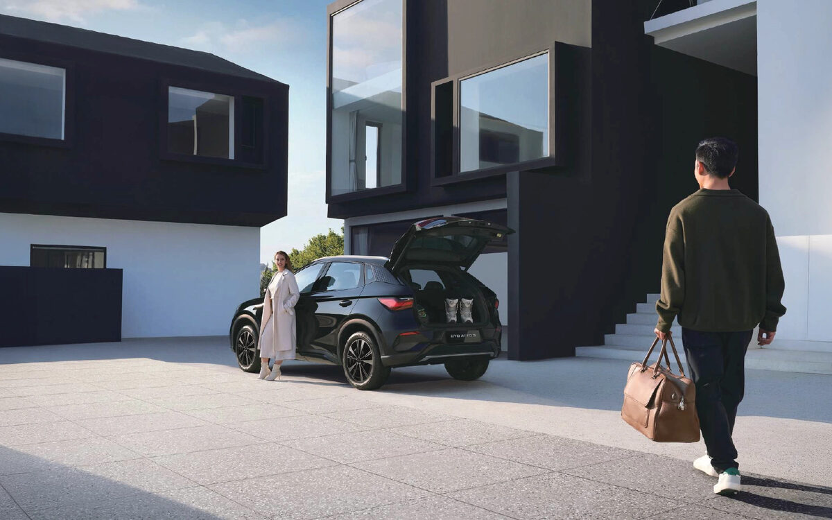 BYD Atto 3 in black with its tailgate open outside a modern house while a man with a bag walks past