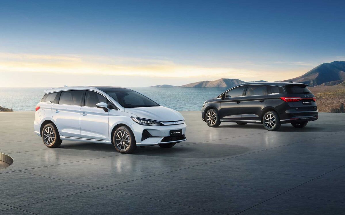 BYD eMAX 7 in white next to a dark one, front three-quarter view on a seaside terrace