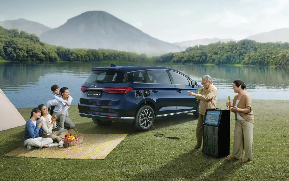 BYD eMAX 7 in blue parked by a lake with a family picnicking beside it