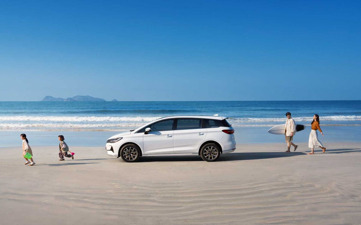 BYD eMAX 7 in white parked on a beach with people walking by