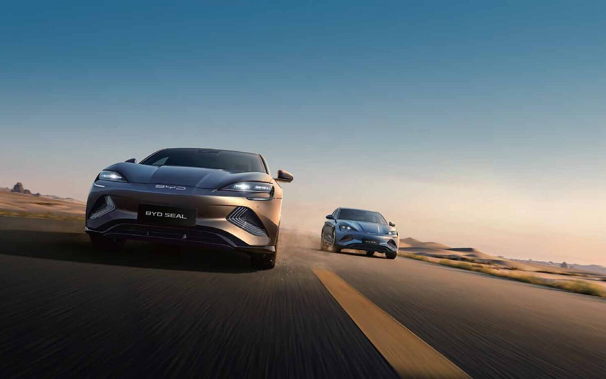 Two BYD Seal cars driving on a desert road at golden hour