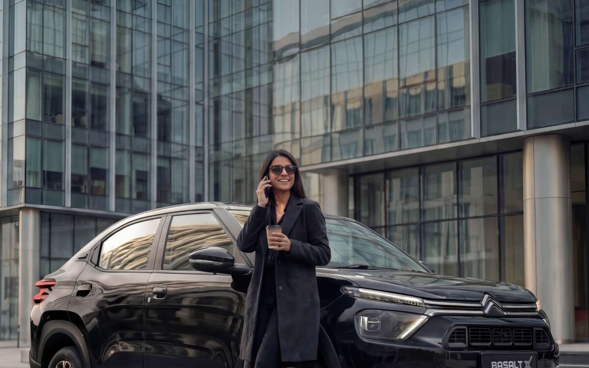 Woman standing beside a black Citroen Basalt in front of a glass office building