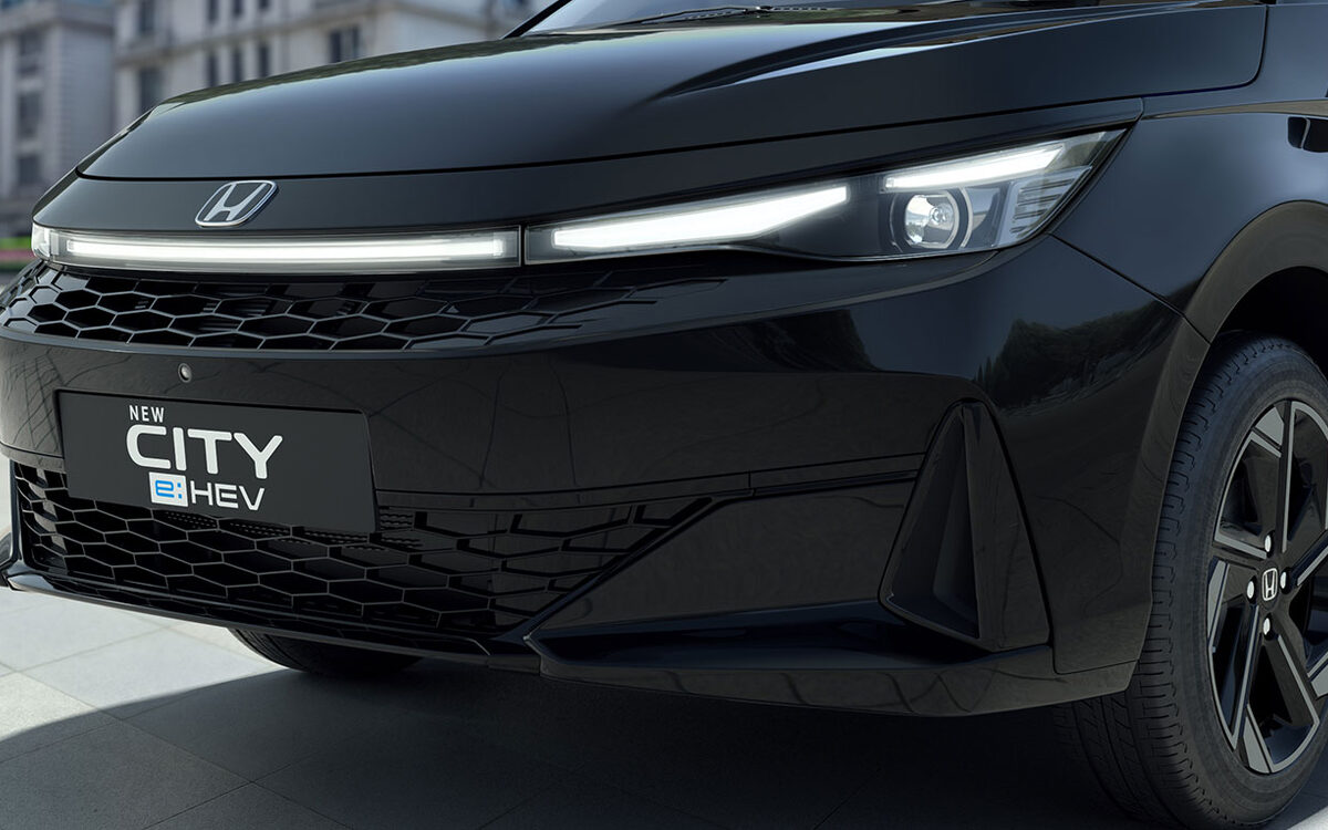 Honda City e:HEV in black, close-up of the front end with the LED light bar, grille and alloy wheel