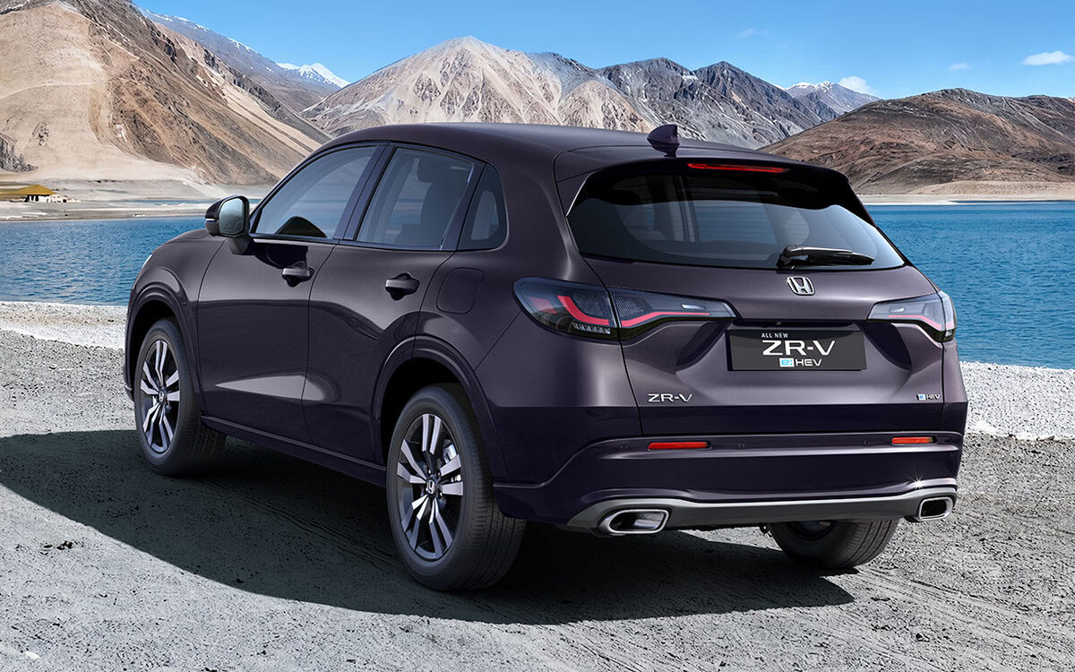 Honda ZR-V e:HEV in dark purple parked by a mountain lake, seen from the rear three-quarter angle
