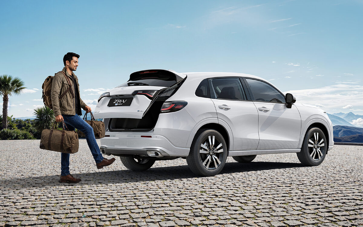 Man carrying bags towards the open tailgate of a white Honda ZR-V on a paved plaza