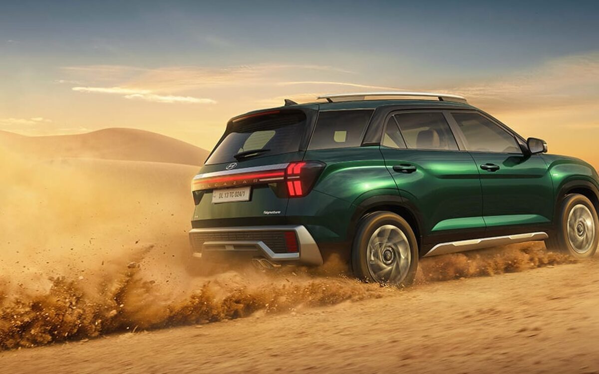 Hyundai Alcazar in green driving across a dune, kicking up sand, rear three-quarter view