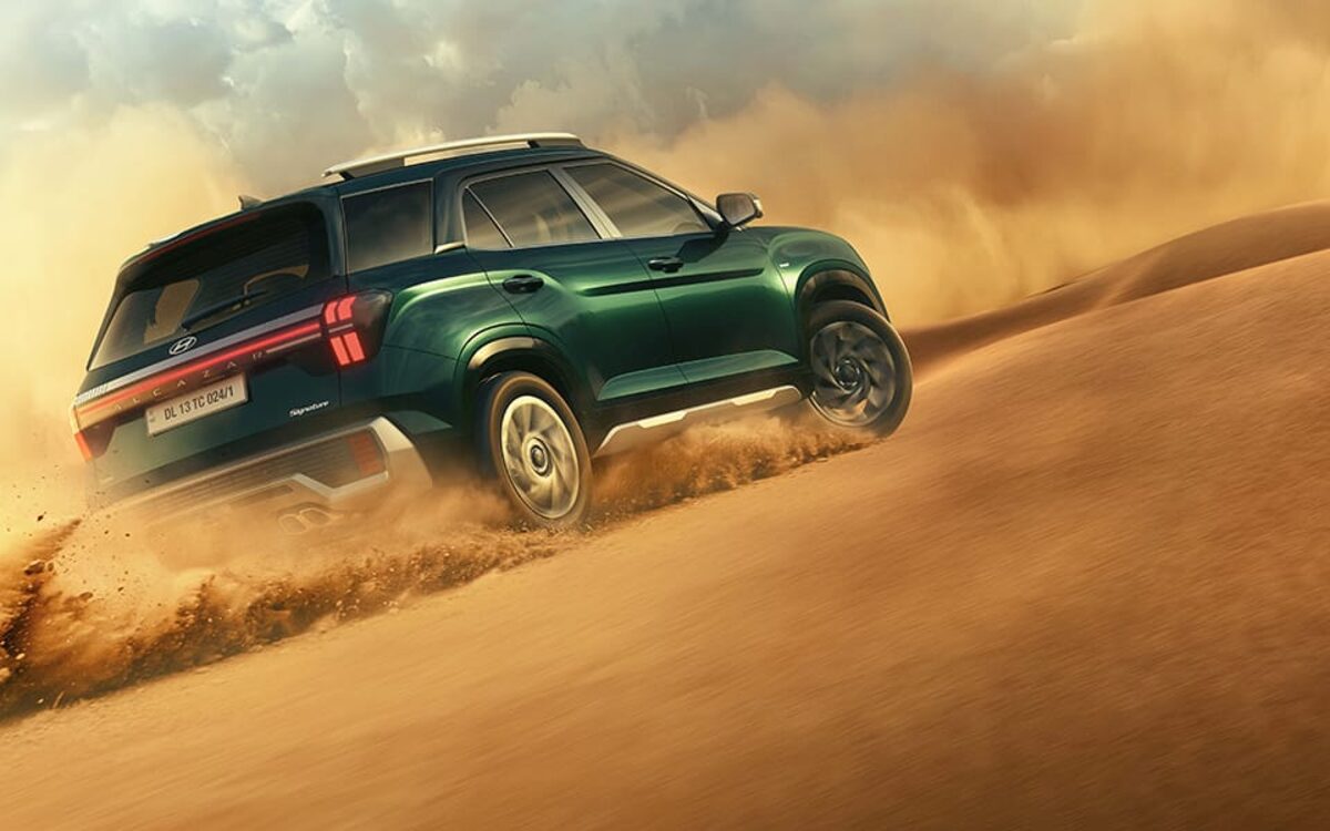 Hyundai Alcazar in green climbing a sand dune with dust flying, front three-quarter view