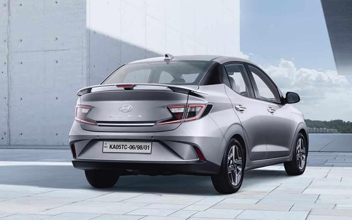 Hyundai Aura in silver, rear three-quarter view against a concrete wall and sky