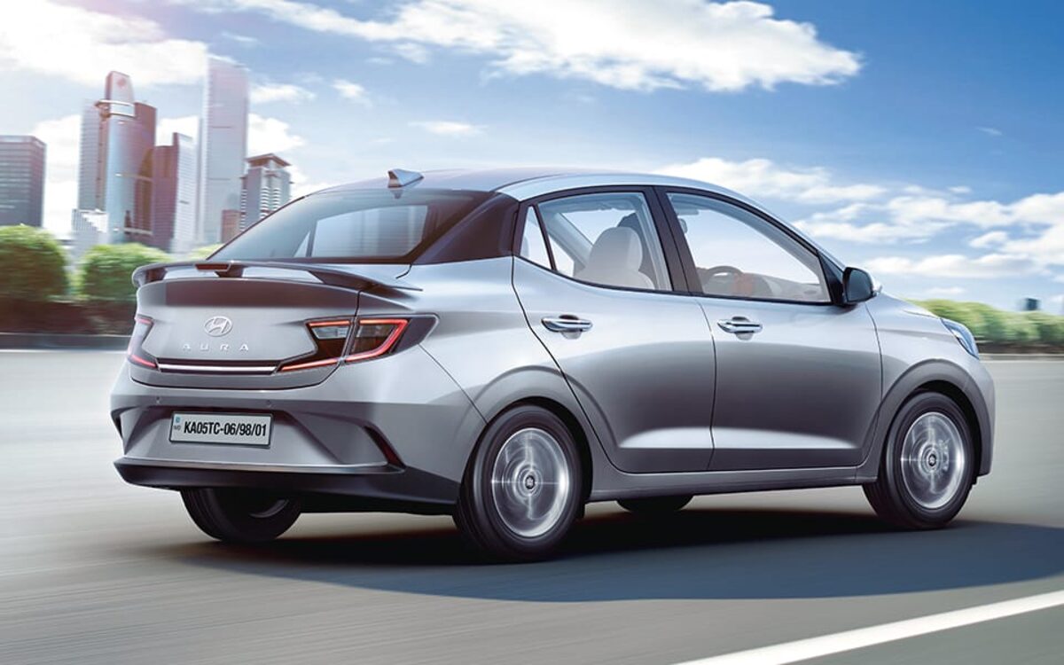 Hyundai Aura in silver driving on a city road, rear three-quarter view