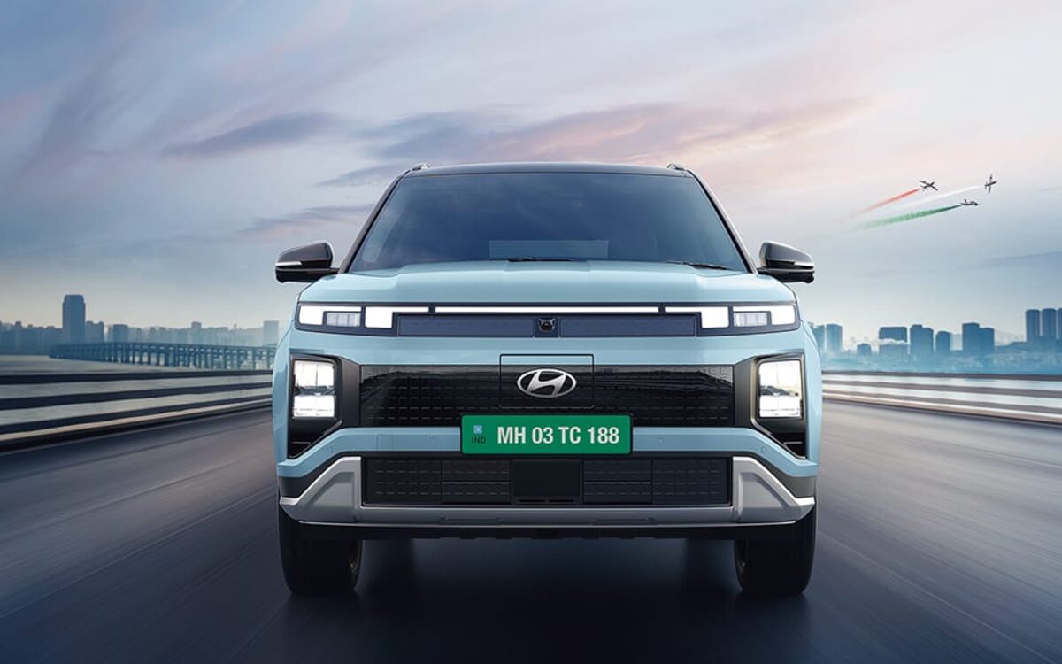 Hyundai Creta Electric in light blue driving towards the camera on a road with a city behind