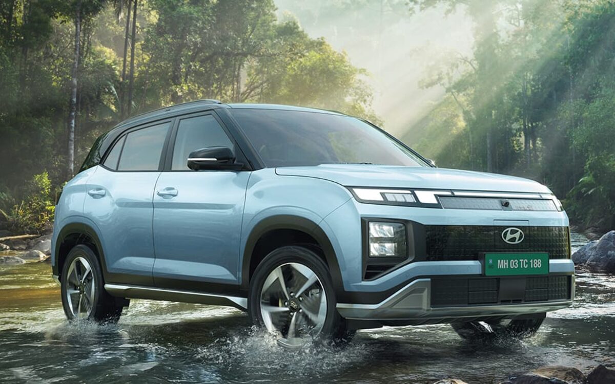 Hyundai Creta Electric in light blue splashing through a shallow river in a forest