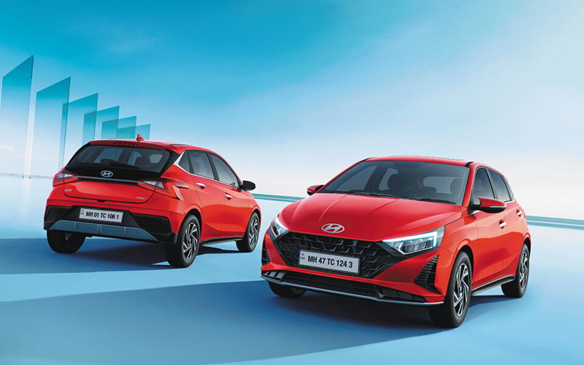 Two Hyundai i20 hatchbacks in red, one seen from the front three-quarter and one from the rear three-quarter, against a blue sky