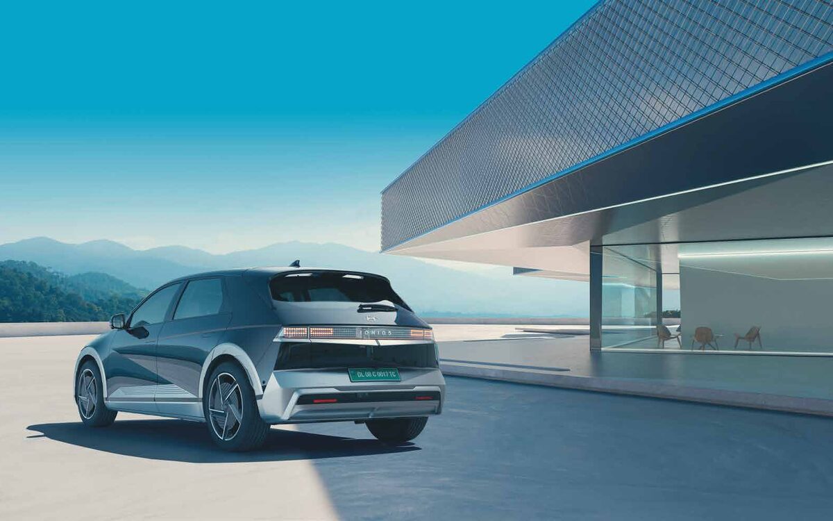 Hyundai IONIQ 5 seen from the rear three-quarter on a terrace beside a modern glass building