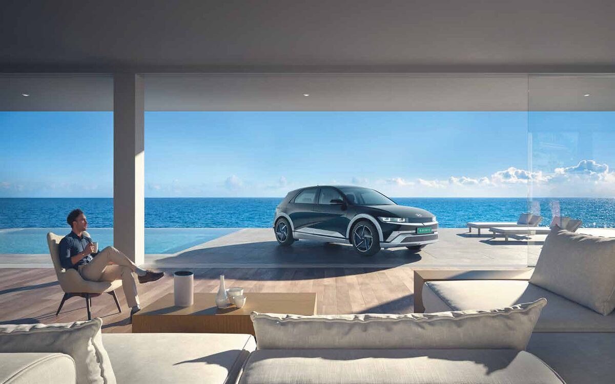 Hyundai IONIQ 5 parked on a seaside deck with a man relaxing in a chair nearby
