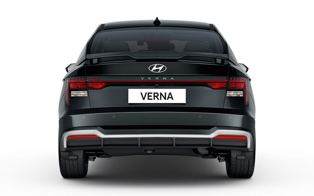 Hyundai Verna in black seen from directly behind, showing the connected tail lamp bar and bumper on a white background