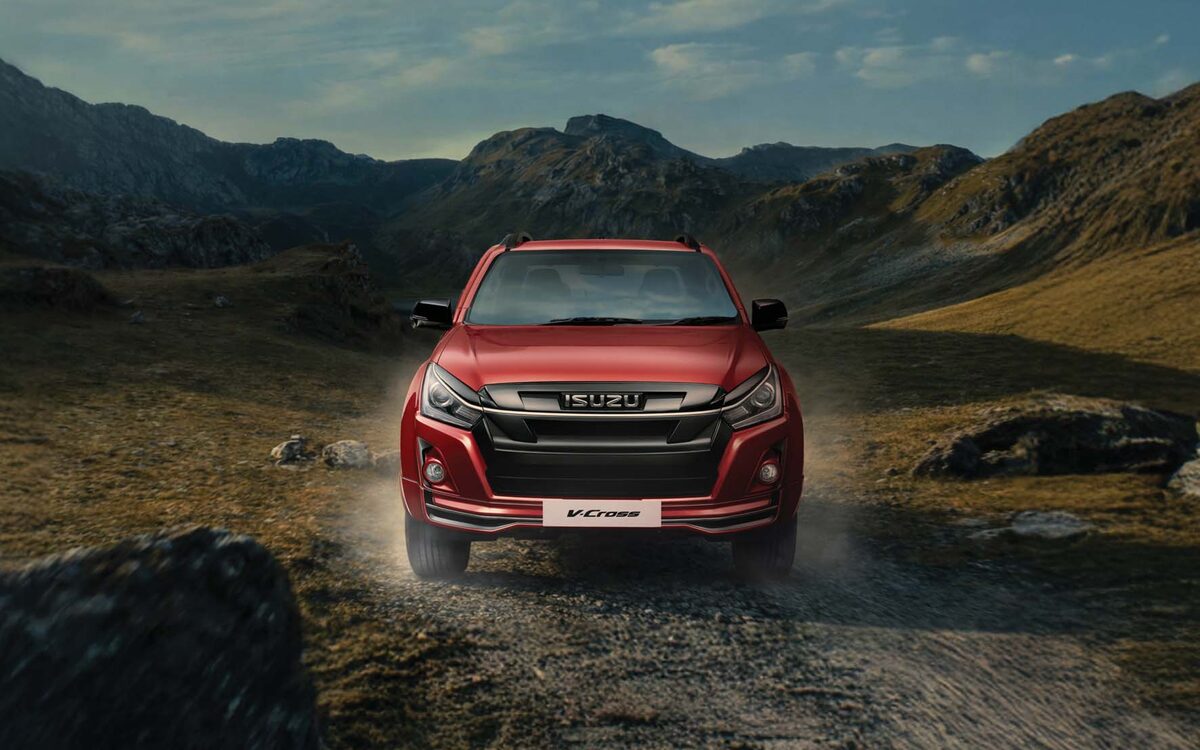 Isuzu D-MAX V-Cross in red driving towards the camera on a dusty valley trail, front view