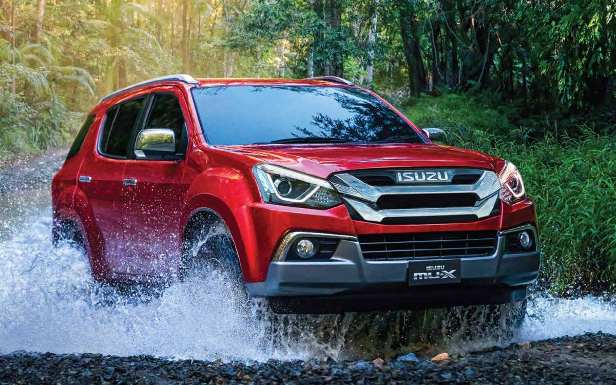Red Isuzu mu-X driving through a splashing stream in a forest