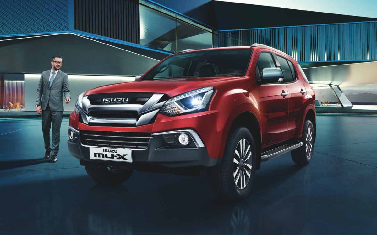 Red Isuzu mu-X in front three-quarter view beside a modern building with a man in a suit standing nearby