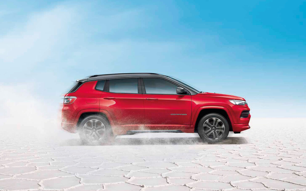 Red Jeep Compass with black roof in side profile on a white salt flat