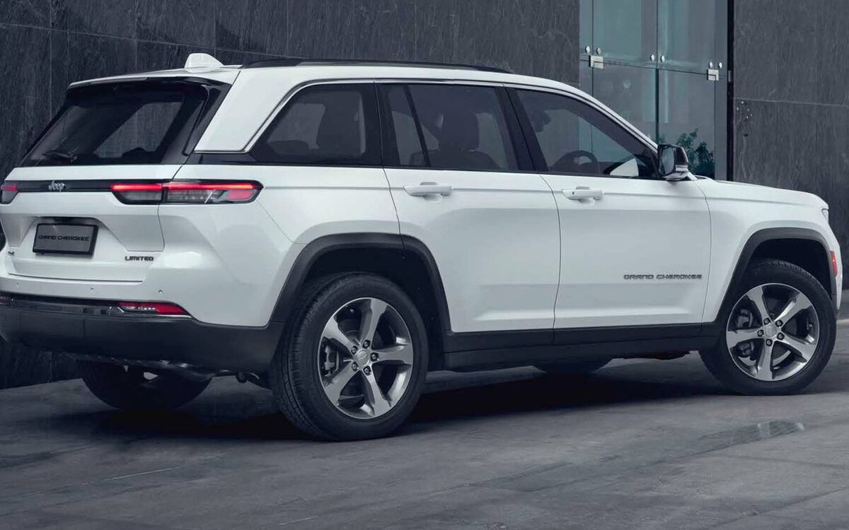White Jeep Grand Cherokee seen from the rear three-quarter beside a dark building