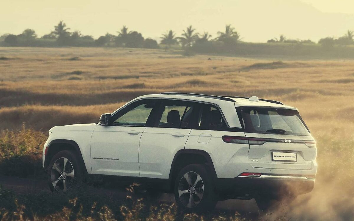White Jeep Grand Cherokee driving across dry grassland, kicking up dust