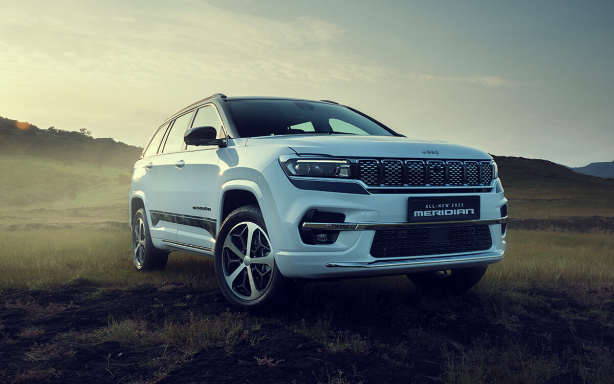 White Jeep Meridian on a grassy hill, front three-quarter view