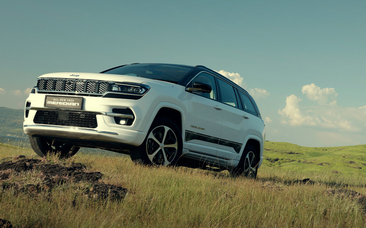 White Jeep Meridian on a rocky grass slope under blue sky