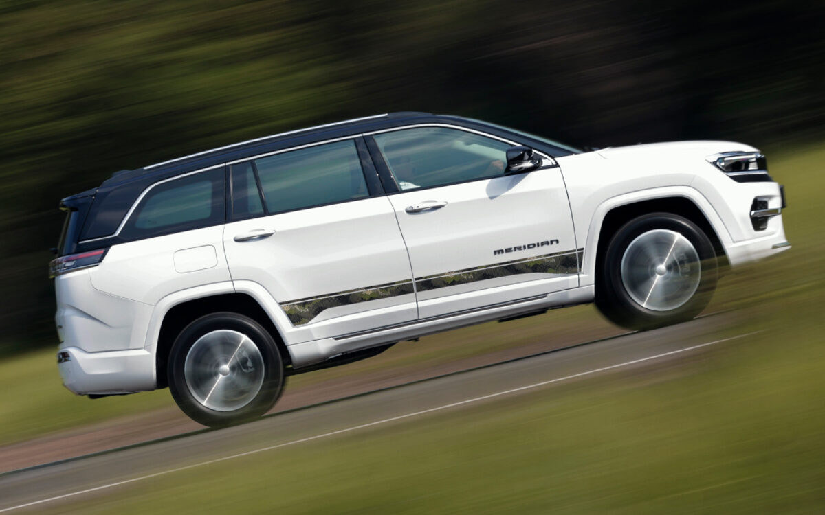 White Jeep Meridian driving along a hill road, side view with motion blur
