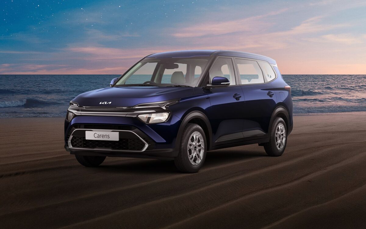 Kia Carens in Imperial Blue on a beach at dusk, front three-quarter view