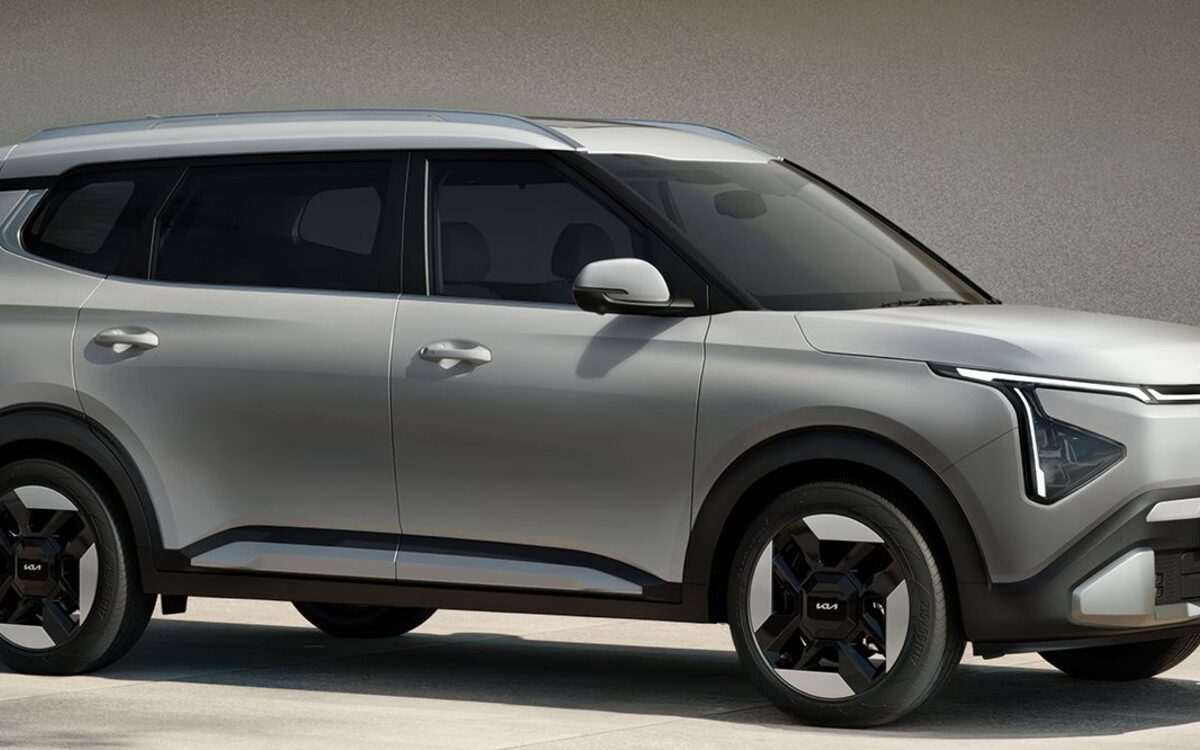Kia Carens Clavis EV seen from the side on a road with dry grass behind