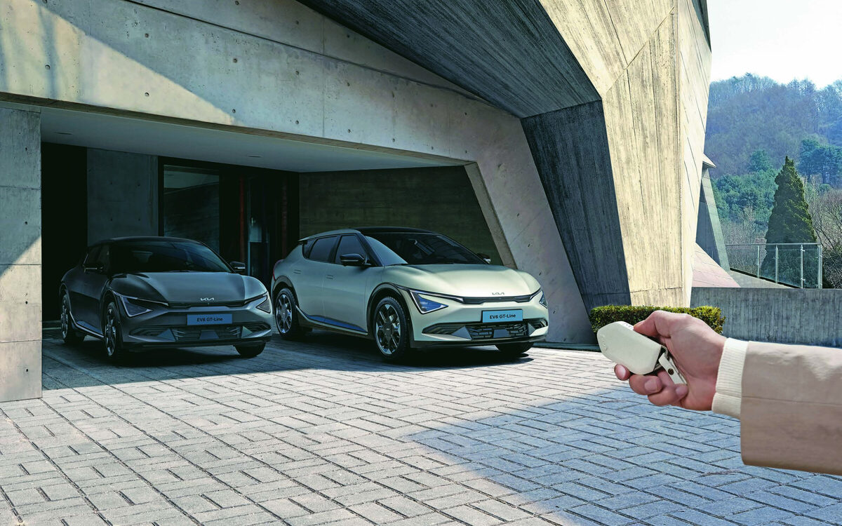 Two Kia EV6 cars parked under a concrete canopy while a hand holds the key fob