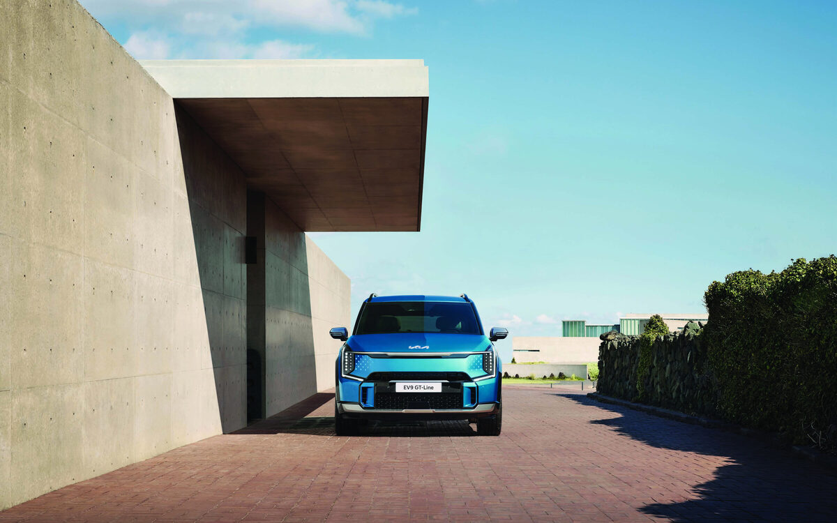 Kia EV9 GT-line in blue driving out from under a concrete building, front view