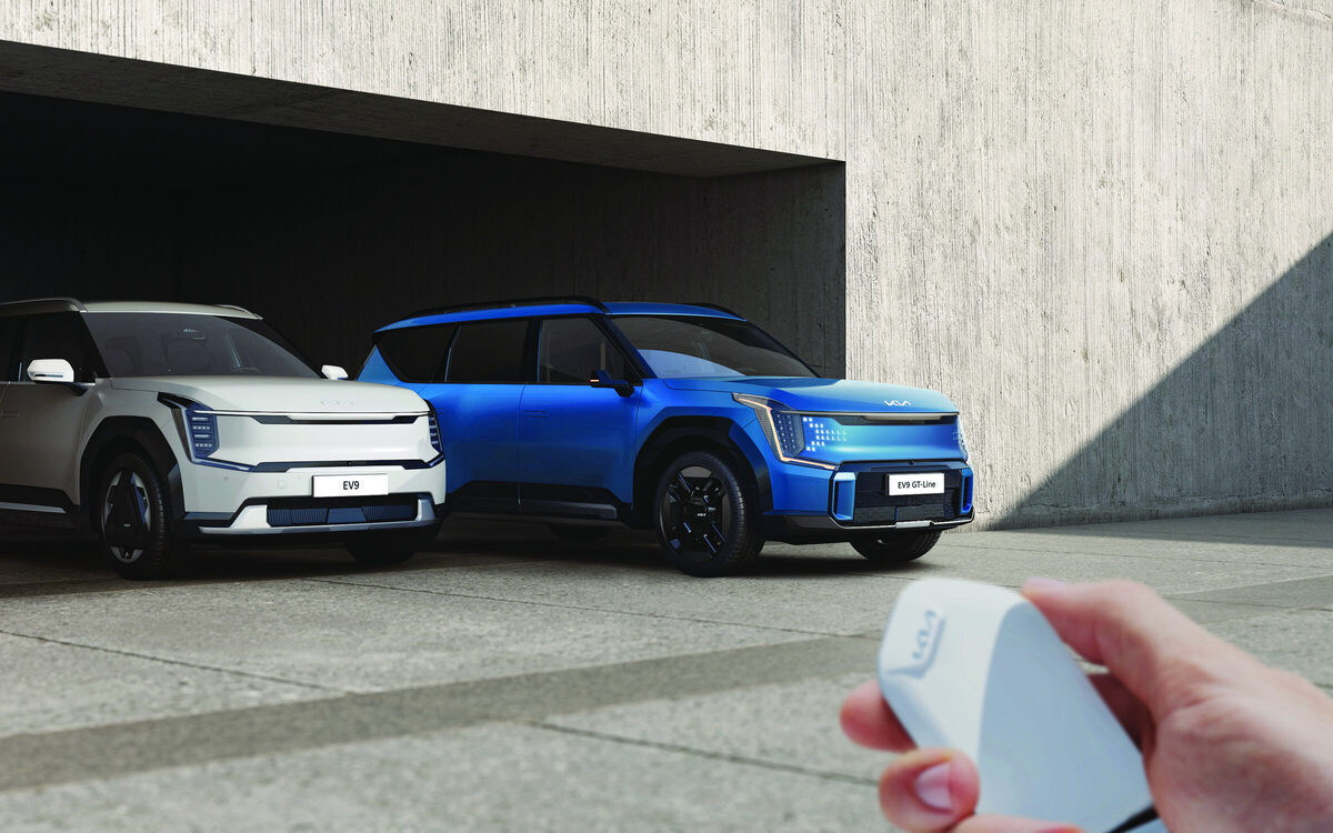 Kia EV9 in blue and light grey parked in a garage while a hand holds the key fob