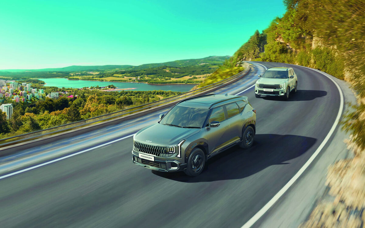 Two Kia Seltos SUVs driving along a curving hill road above a lake