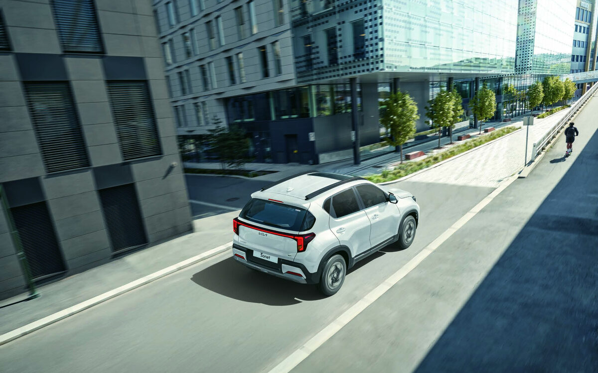 Kia Sonet in white driving away on a city street, seen from above and behind