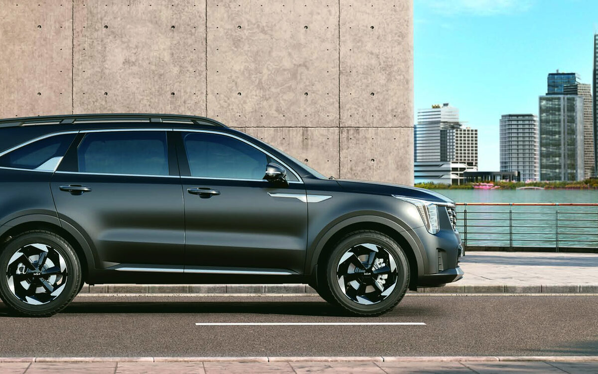 Kia Sorento in dark grey, side profile on a city waterfront road with a concrete wall and high-rise buildings behind