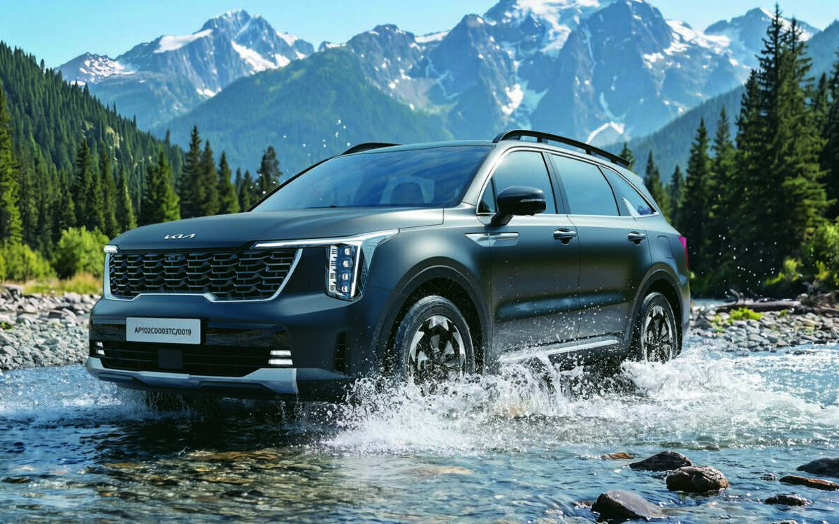 Kia Sorento in dark grey driving through a shallow mountain stream with water splashing, forest and snowy peaks behind