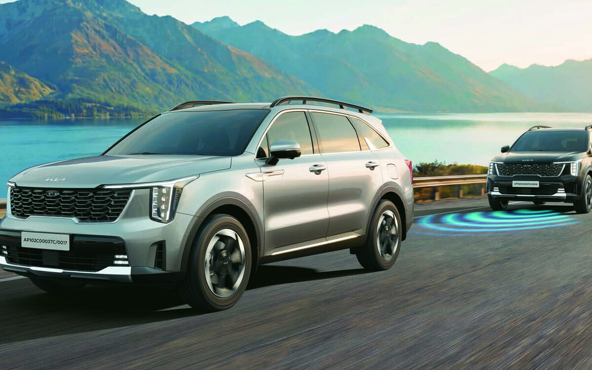 Kia Sorento in silver, front three-quarter view driving on a coastal mountain road with another Sorento behind it and a blue sensor graphic on the road
