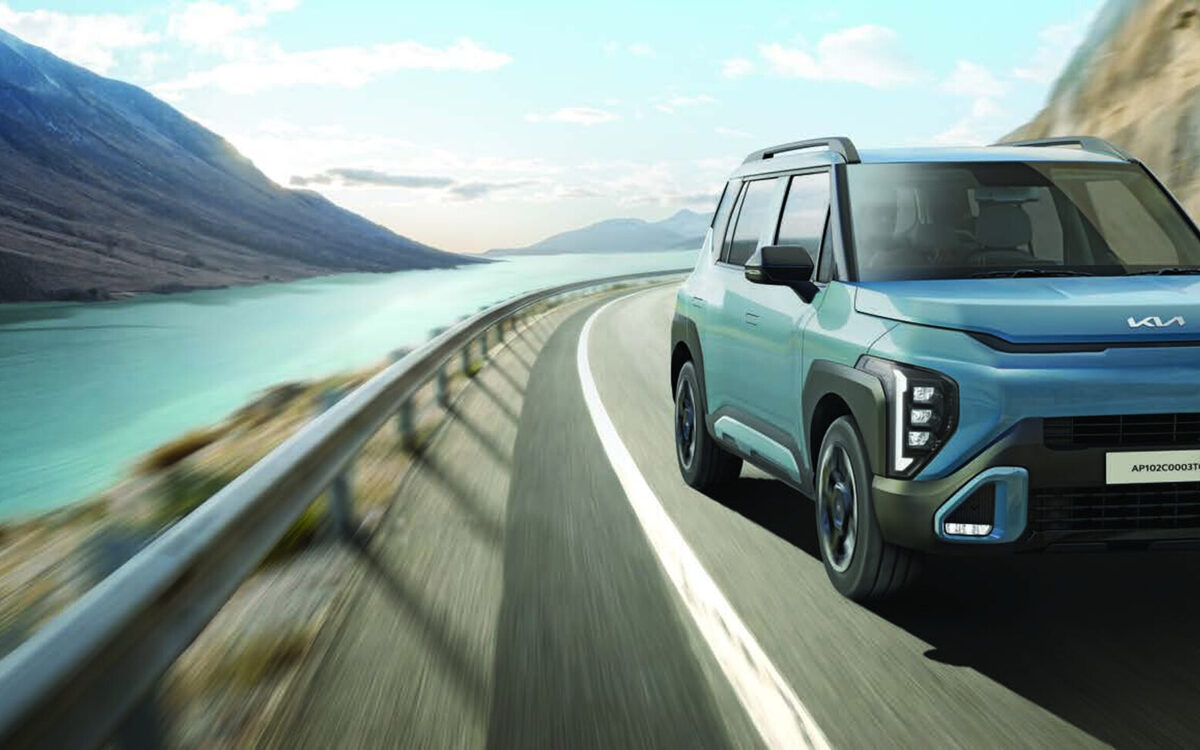 Frost Blue Kia Syros driving along a curved lakeside mountain road, front view