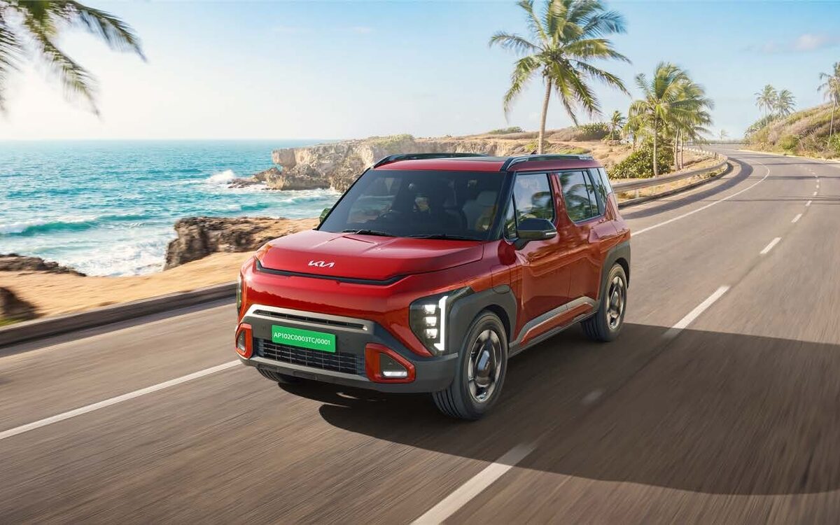 Kia Syros EV in red driving along a seaside road with palm trees