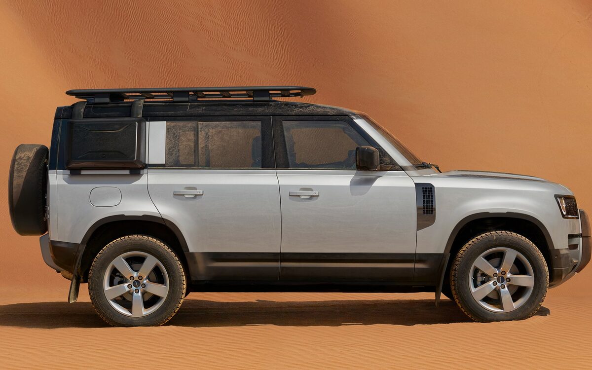 Land Rover Defender in silver with a roof rack, side profile against an orange backdrop