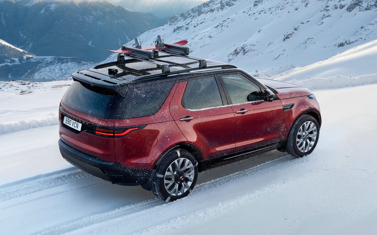 Land Rover Discovery in red, rear three-quarter view on a snowy mountain road with ski rack
