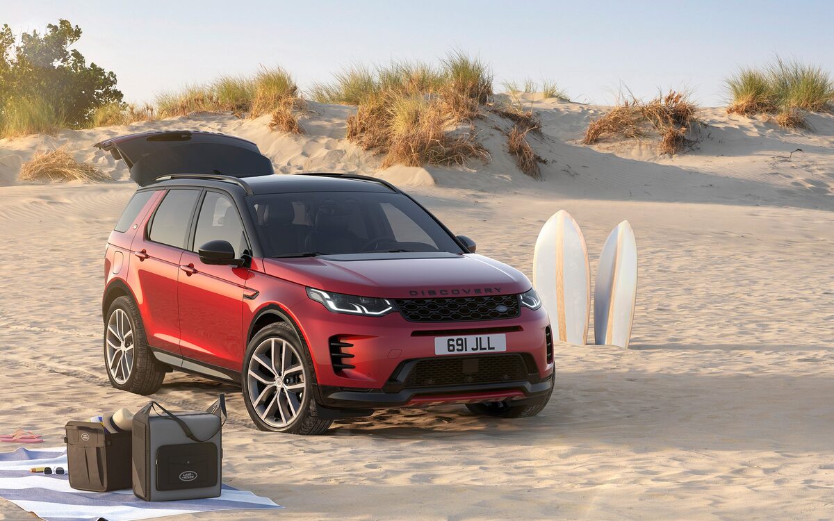 Land Rover Discovery Sport in red parked on a sandy beach with surfboards