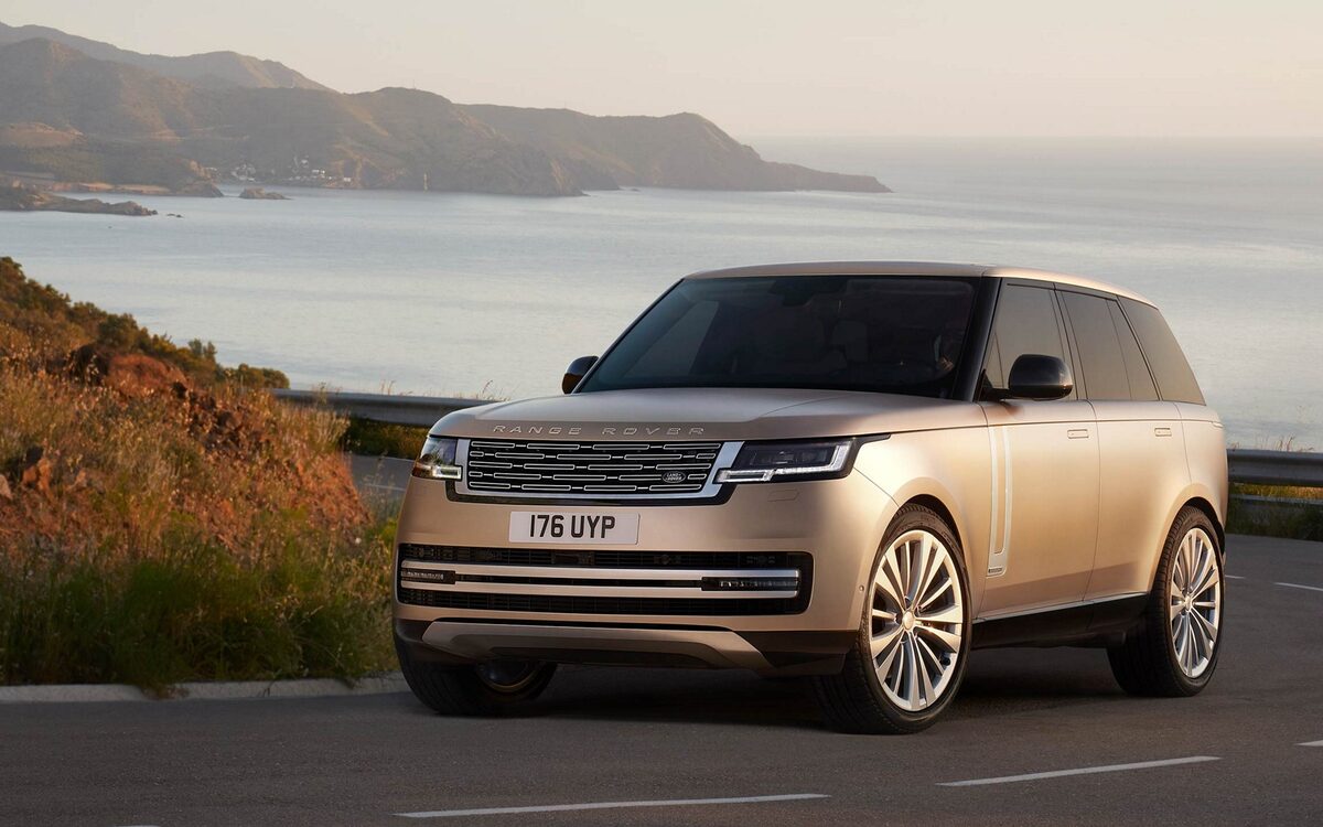 Range Rover in gold driving along a coastal road, front three-quarter view