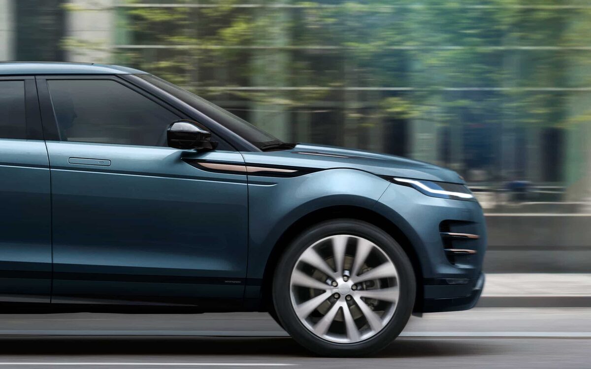 Range Rover Evoque in blue driving past city buildings, side view of the front half