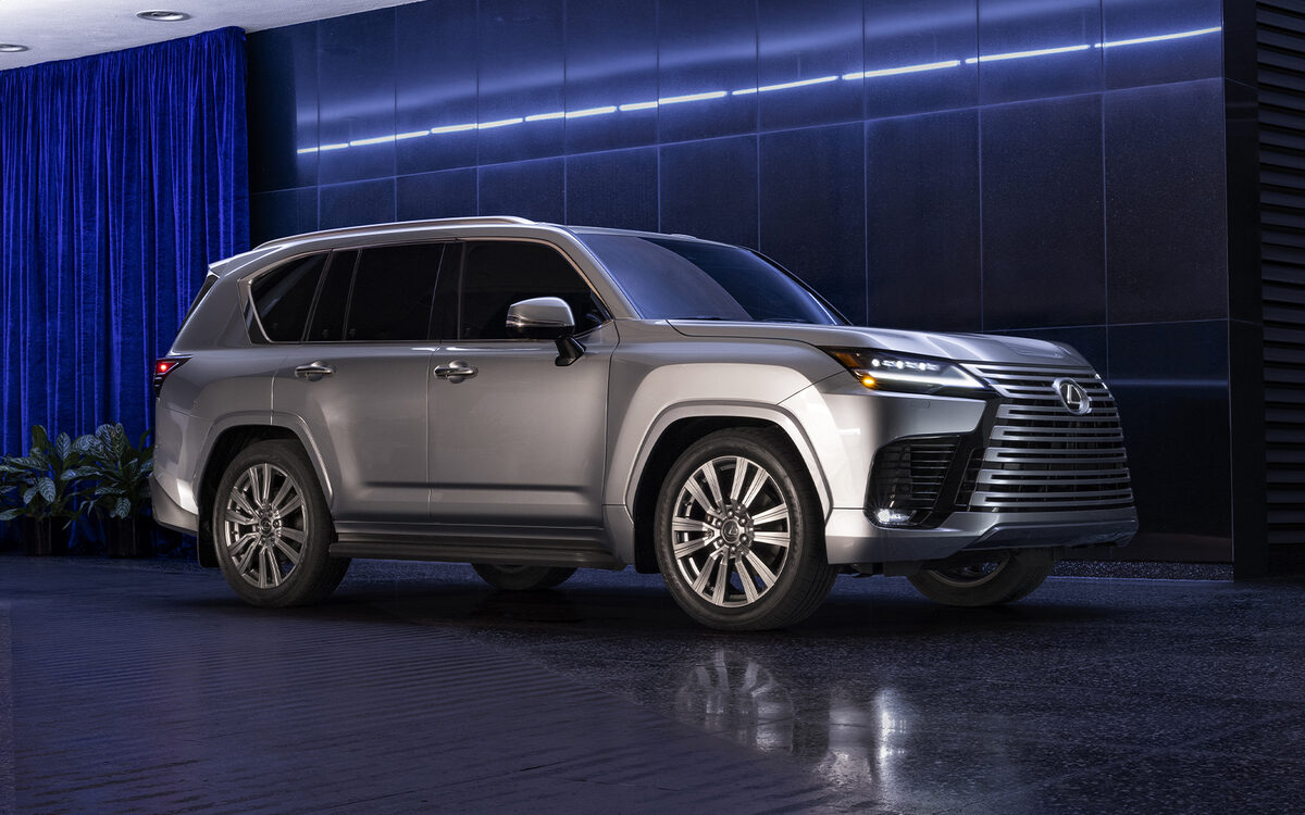 Lexus LX in grey parked in front of a blue-lit building at night, front three-quarter view