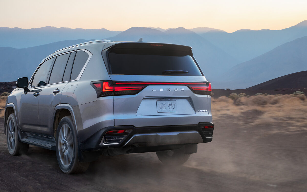 Lexus LX driving along a dusty mountain road seen from the rear three-quarter